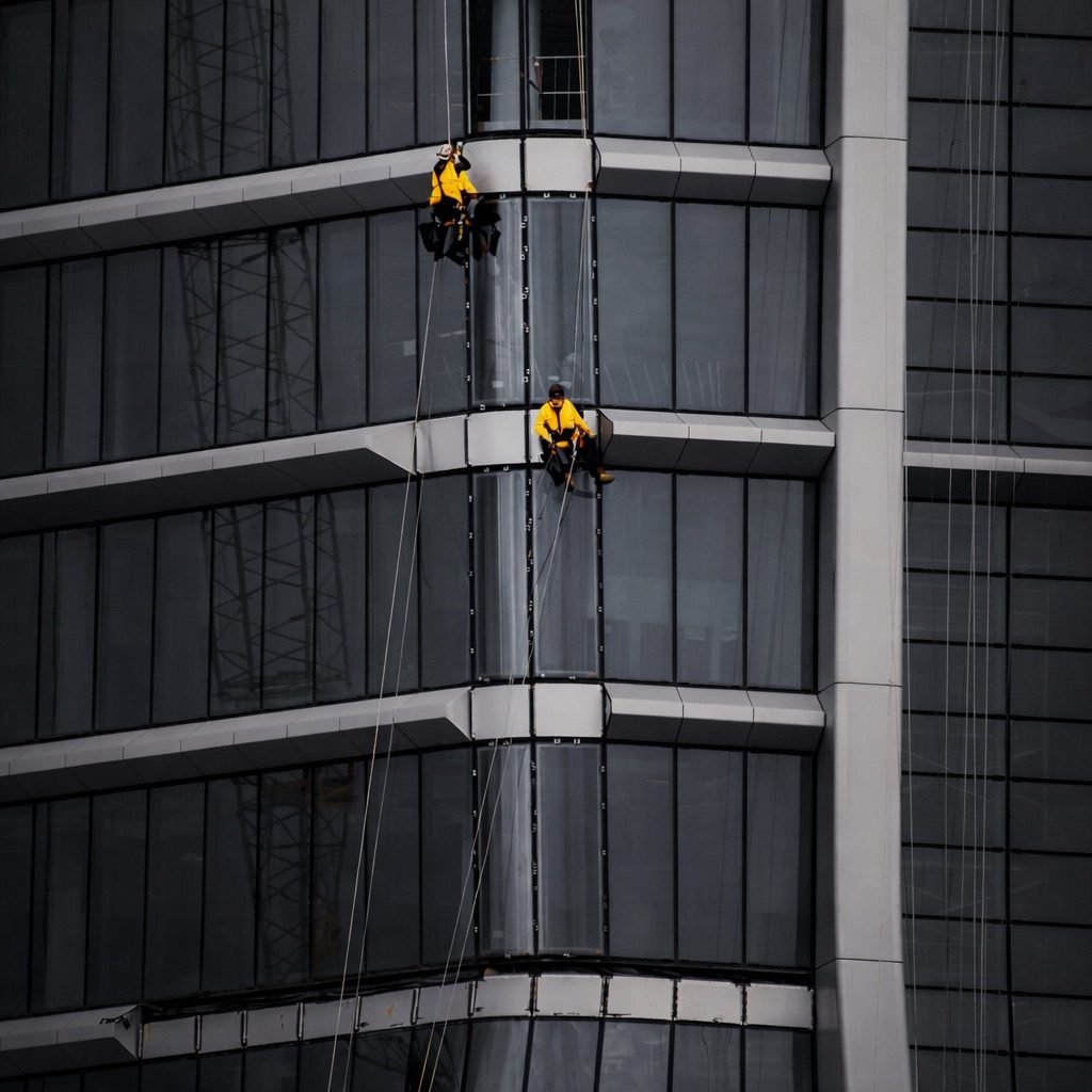 Höhenarbeit Zwei Arbeiter reinigen die Fenster an einem modernen Hochhaus. Höhenarbeit Industrieklettern Fenster Hochhaus reinigen